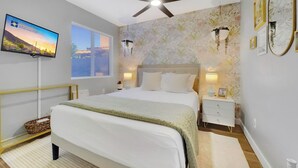 A bedroom with a bed, bedside tables, a ceiling fan, a TV, and a window with blinds. - Yucca Mesa (Mesa)