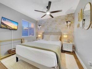 A bedroom with a bed, bedside tables, a ceiling fan, a TV, and a window with blinds. - Yucca Mesa (Mesa)