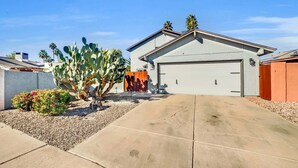 A residential garage with a white door, a driveway leading to the garage, and a large cactus in the front yard. - Yucca Mesa (Mesa)