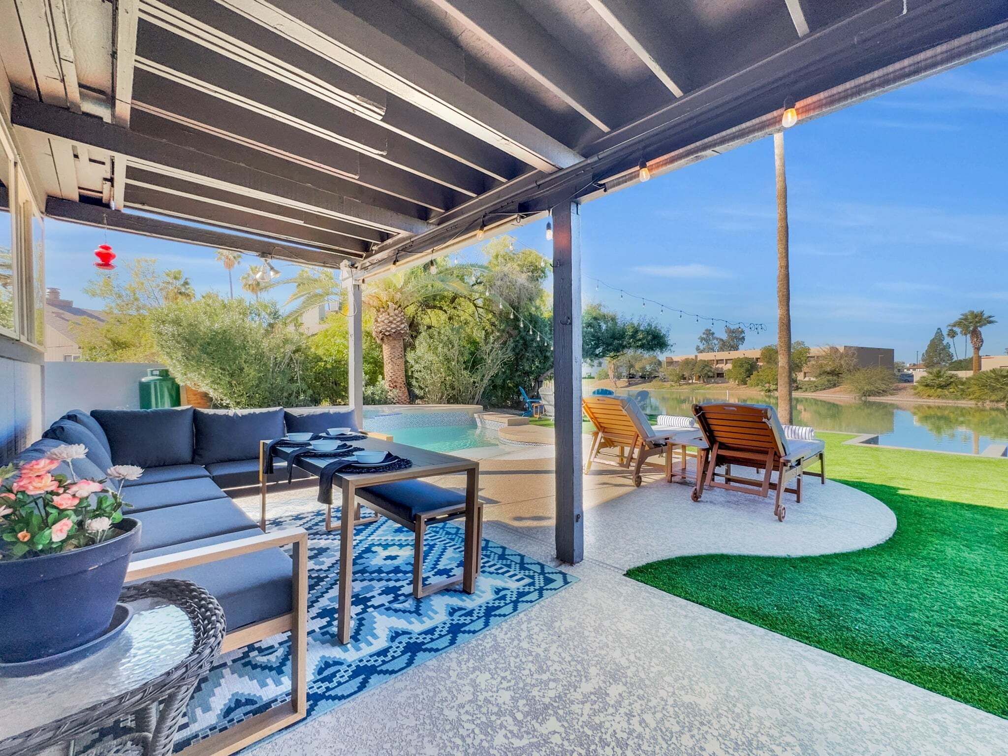 A covered outdoor area with a pool, lounge chairs, and a dining setup.