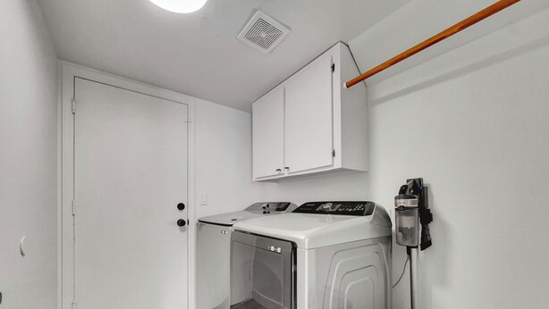 A laundry room with a front-loading washer and dryer, a white cabinet above the dryer, and a laundry basket on the floor. - Delta Mesa (Mesa)