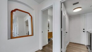 A hallway with white walls, a wooden floor, and a mirror with a wooden frame. - Delta Mesa (Mesa)