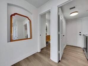 A hallway with white walls, a wooden floor, and a mirror with a wooden frame. - Delta Mesa (Mesa)