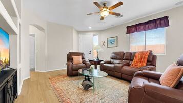 A living room with a ceiling fan, a brown leather sofa, a glass coffee table, and a patterned rug.