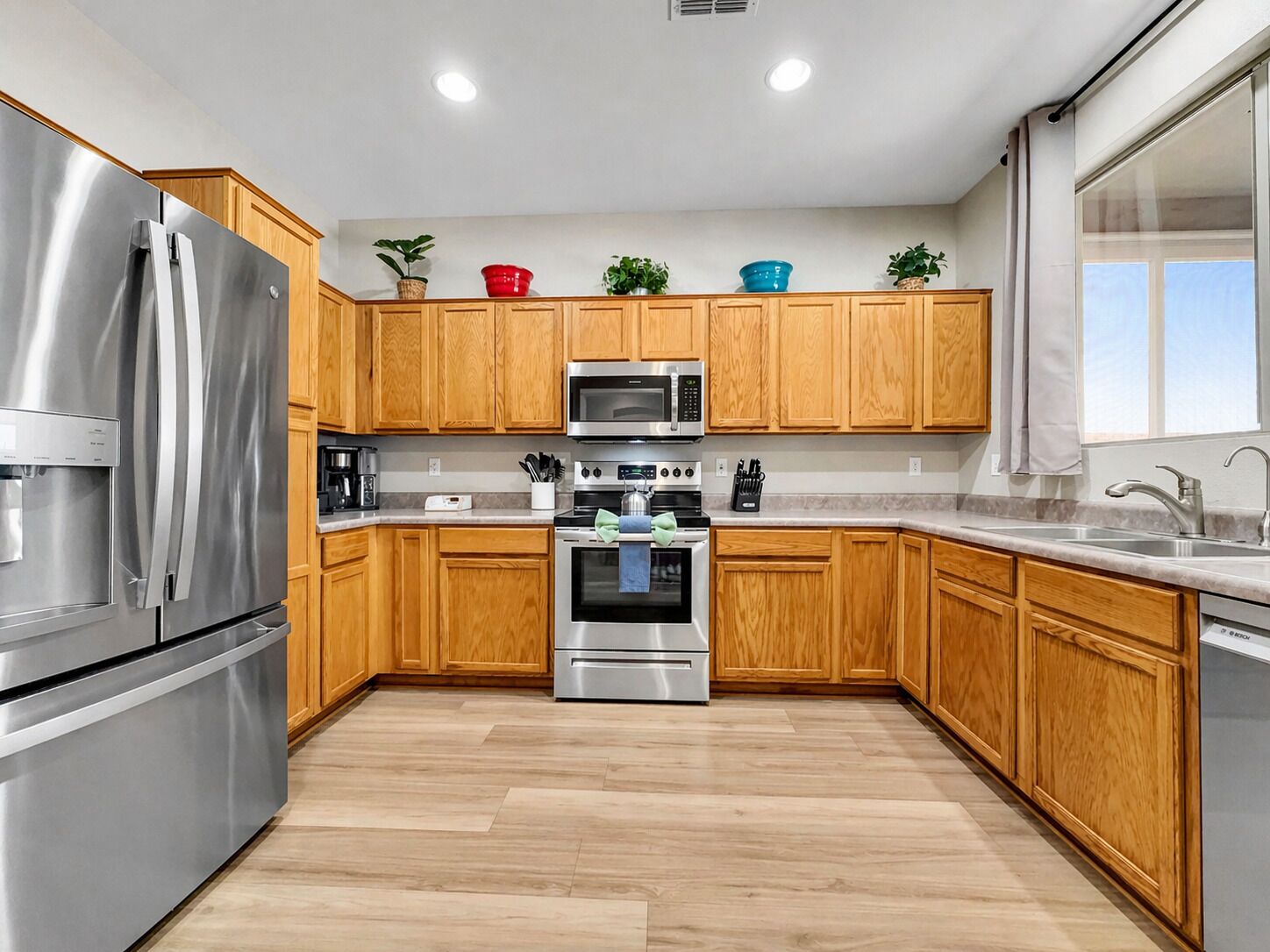 A modern kitchen with wooden cabinets, stainless steel appliances, and a large window.