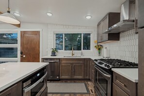 A modern kitchen with stainless steel appliances, a large window, and a view of the outdoors. - Relaxing Mid-Century Home Near Ski Resorts with SwimSpa & EV Charger (Cottonwood Heights)