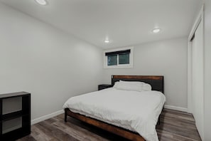 Ein Schlafzimmer mit einem Bett, einem Nachttisch, einem Fenster und einer Deckenleuchte.
