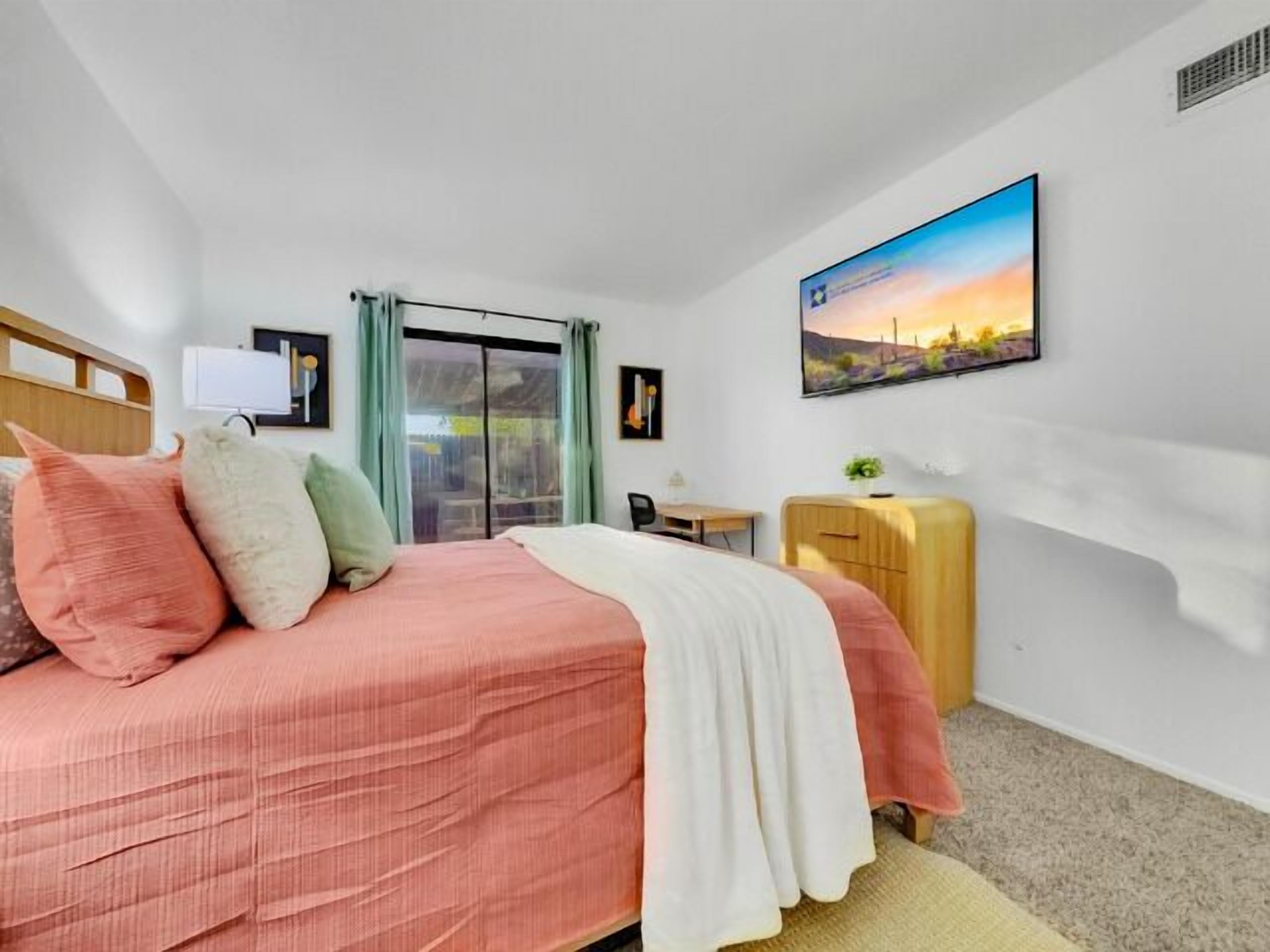Une chambre à coucher comprenant un lit, un bureau, une chaise, une armoire, une fenêtre avec des rideaux et un tableau accroché au mur.