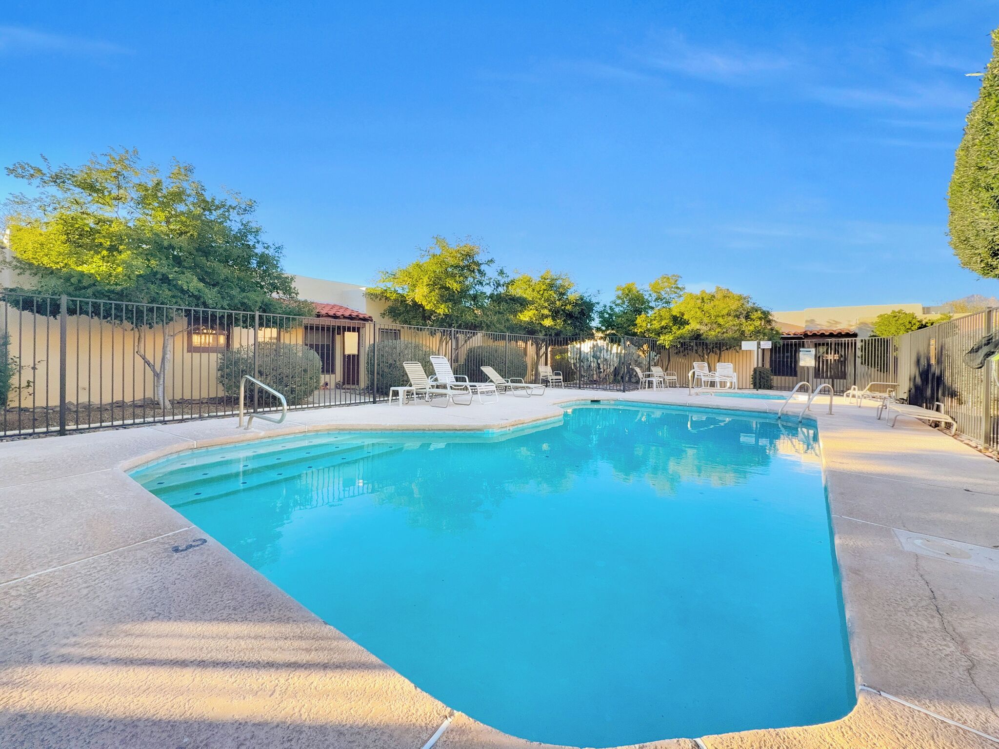 A swimming pool with a curved edge, surrounded by a fence, and equipped with lounge chairs.