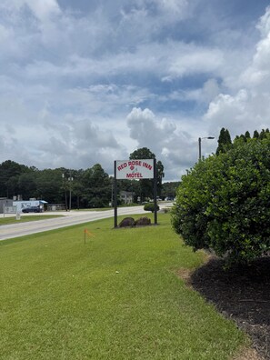 A motel sign, a road, and a grassy area with a bush. - RED ROSE INN MOTEL (Bremen)