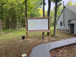 A wooden signboard in a wooded area with a metal speaker stand beside it. - Fish and Swim: Home w/ Catskill Creek Views! (East Durham)