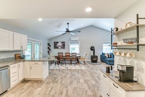 A modern kitchen with white cabinets, a dining area with a table and chairs, a built-in wood stove, and a ceiling fan. - Fish and Swim: Home w/ Catskill Creek Views! (East Durham)