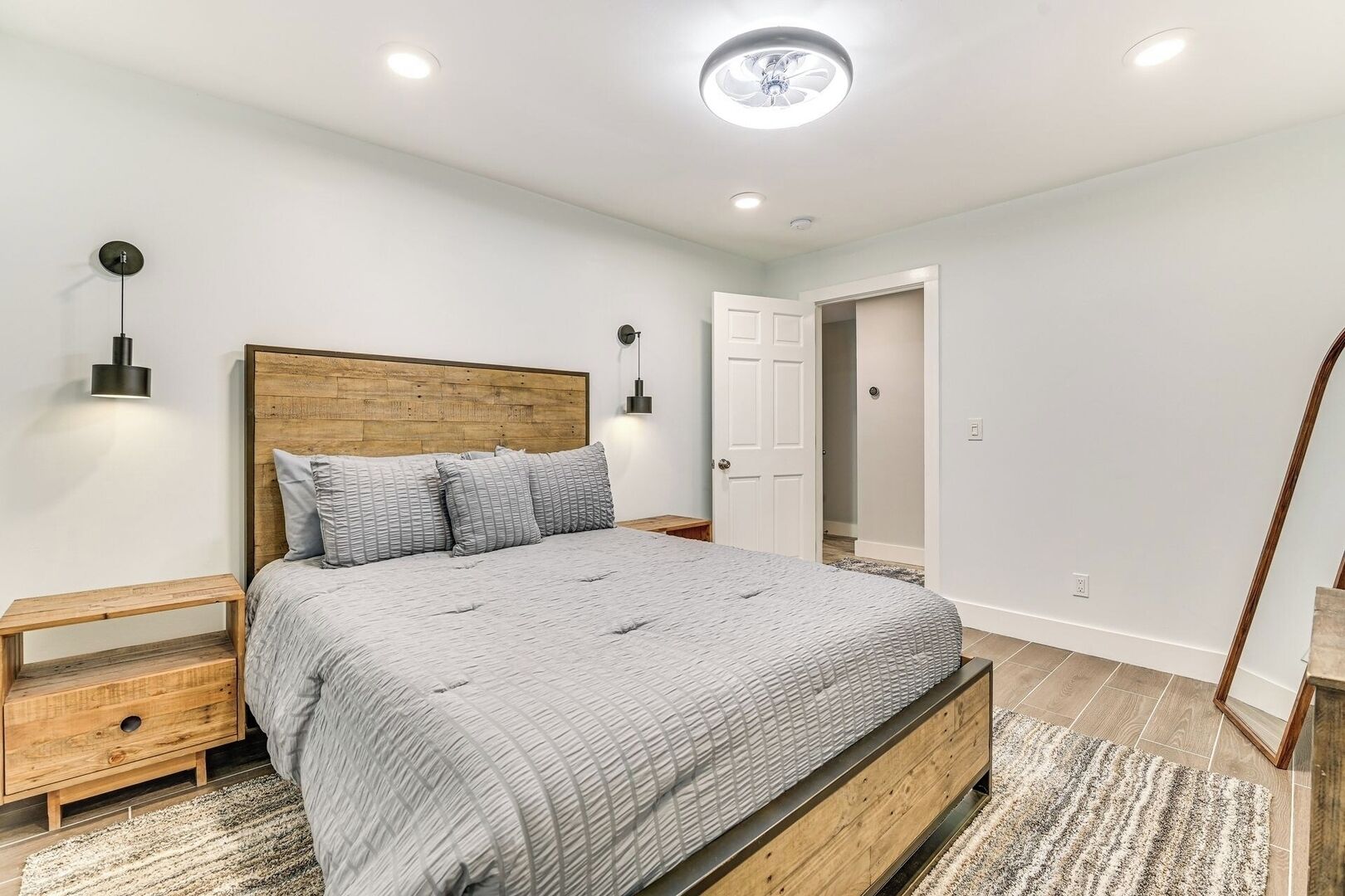 Une chambre à coucher comprenant un lit, des tables de chevet, une tête de lit en bois, une porte et un luminaire au plafond.