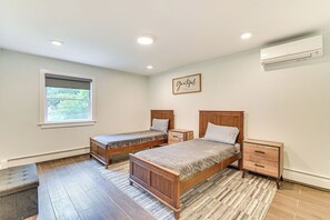 A bedroom with two wooden beds, a window, a wall-mounted air conditioner, and a rug. - Fish and Swim: Home w/ Catskill Creek Views! (East Durham)