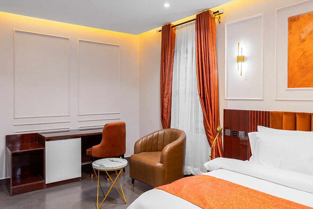 A hotel room with a bed, a desk, two chairs, a small table, and a wall-mounted light.