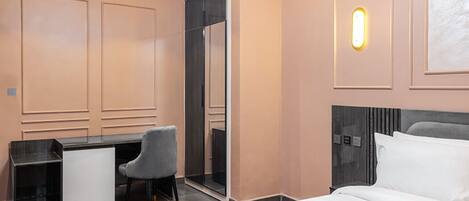 Habitación de hotel con cama, escritorio, silla, armario y una lámpara de pared.