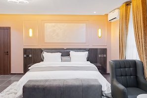 A modern bedroom with a large bed, a chair, and a wall-mounted air conditioner.