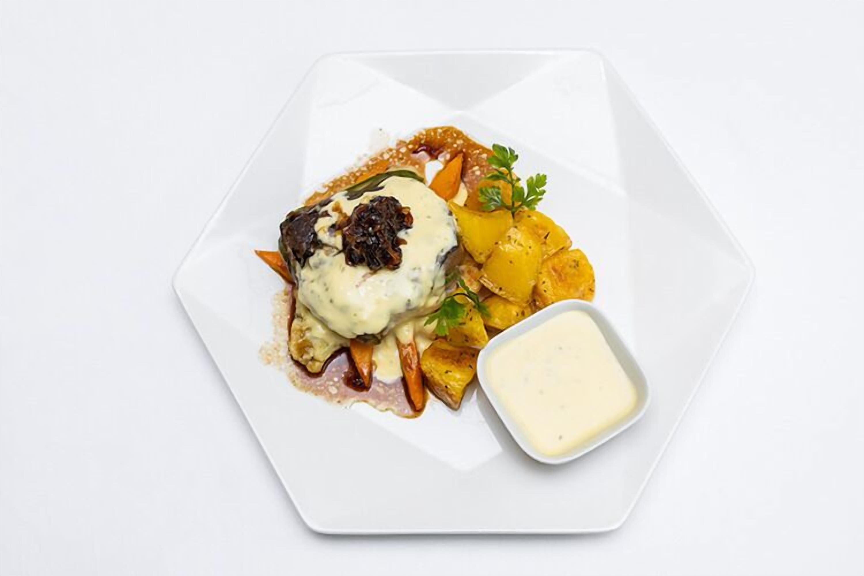 A white plate with a dish of meat, vegetables, and sauce, and a small bowl of sauce.