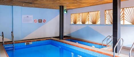 An indoor swimming pool with clear water, wooden ceiling, and safety signs on the walls.