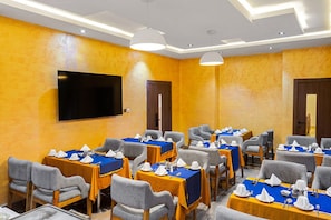 A hotel room with multiple tables and chairs, a flat-screen TV, and a door. - BON Hotel Emporium (Ughelli)