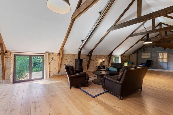 A spacious loft with exposed wooden beams, a fireplace, leather sofas, and a large sliding glass door. - Holiday Home 'Folperdrix' with Private Terrace and Garden (Surzur)