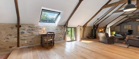 A spacious loft with exposed wooden beams, a stone wall, and a wooden floor.