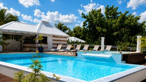 Une piscine avec des chaises longues, un espace de repos couvert et un bâtiment portant une enseigne.