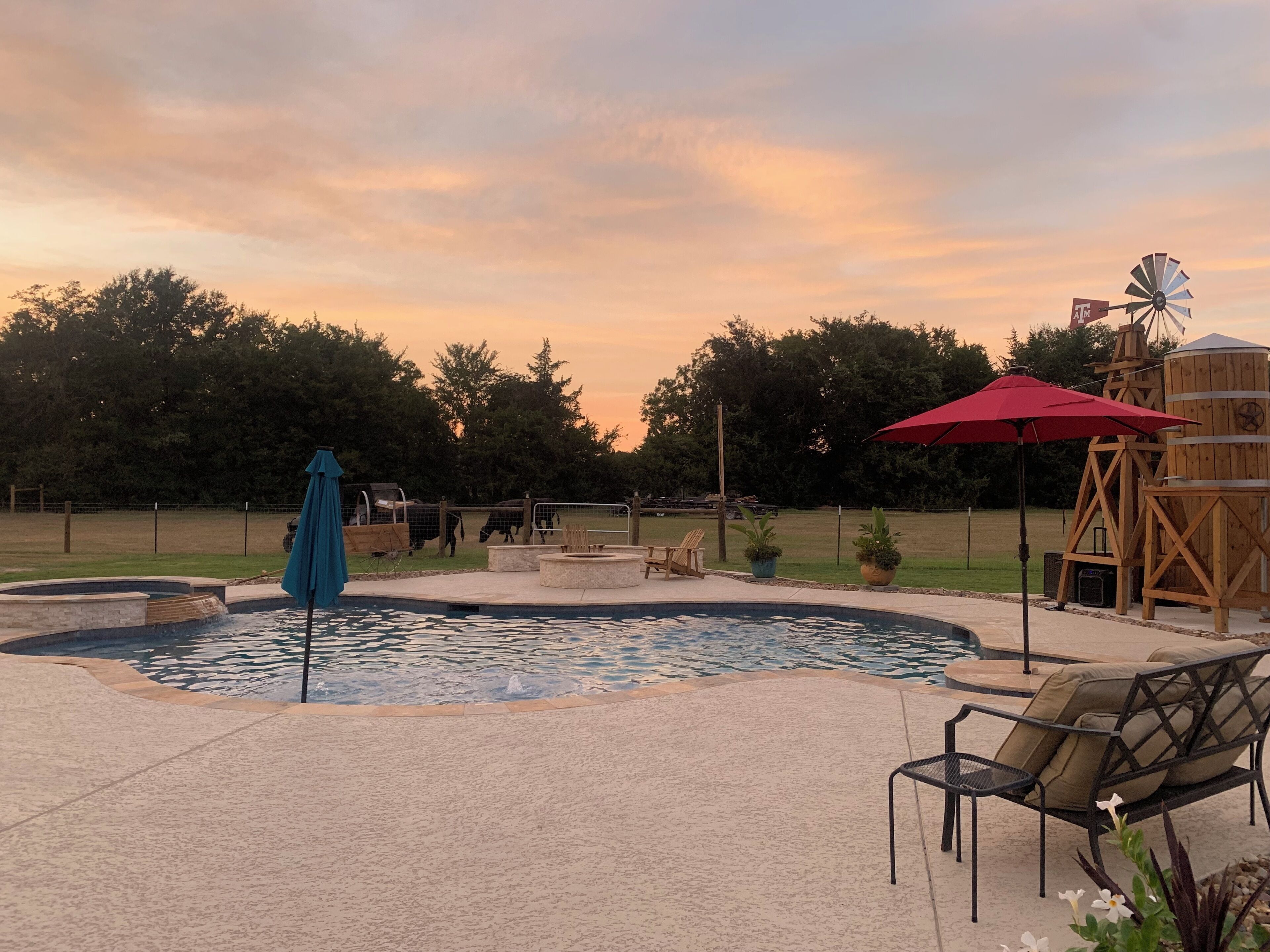 A pool area with a windmill, outdoor furniture, and a fenced enclosure with animals.