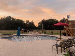 A pool area with a windmill, outdoor furniture, and a fenced enclosure with animals. - Beautiful 2-bedroom Casita with a country feel and fluffy cows (Bryan)