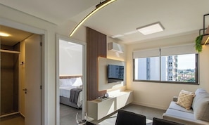 Une chambre d’hôtel moderne équipée d’un lit, d’un bureau, d’une télévision et d’une grande fenêtre donnant sur la ville.