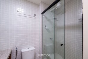Ein Badezimmer mit weißen Fliesen, einer Glasdusche, einer Toilette und einem Handtuchhalter.