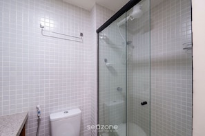Ein Badezimmer mit weißen Fliesen, einer Glasdusche, einer Toilette und einem Handtuchhalter.