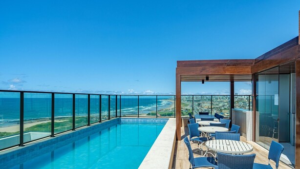 A rooftop pool with a view of the ocean and cityscape, furnished with outdoor seating. - Studio in Cond. With Pool and gym Soa0906 (Salvador)