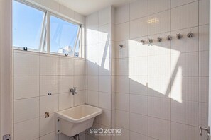 A bathroom with white tiled walls, a window, a sink, and a shower with multiple faucets. - Penthouse w/ Balcony Near the Beach Acu0044 (Ubatuba)