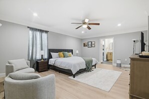 Ein Schlafzimmer mit Bett, Sessel, Nachttisch, Deckenventilator, Lampe und Kleiderschrank.