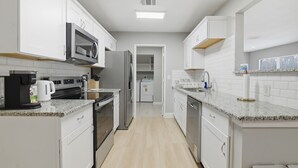 Una cocina moderna con armarios blancos, microondas, refrigerador y lavavajillas.