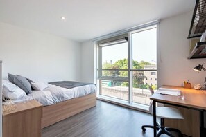 Ein modernes Schlafzimmer mit Bett, Schreibtisch und großem Fenster.