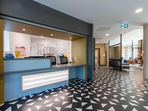 A reception desk with a modern design, a patterned floor, and a visible emergency exit sign. - Student Only Print Hall (Underpass)