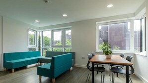 Ein modernes Zimmer mit einer Eckcouch, einem Esstisch mit Stühlen und großen Fenstern mit Blick auf die Stadt.