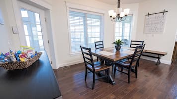 A dining area with a wooden table and chairs, a chandelier, and a basket of snacks on the counter.