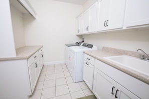 A laundry room with a washing machine, a sink, and cabinets. - Beautiful 4-Bedroom Modern Farmhouse located outside of Saint Joseph, IL (Saint Joseph)