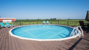 An outdoor swimming pool with a wooden deck, surrounded by a metal fence, and a clear view of the countryside. - Beautiful 4-Bedroom Modern Farmhouse located outside of Saint Joseph, IL (Saint Joseph)