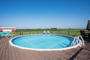 An outdoor swimming pool with a wooden deck, surrounded by a metal fence, and a clear view of the countryside. - Beautiful 4-Bedroom Modern Farmhouse located outside of Saint Joseph, IL (Saint Joseph)