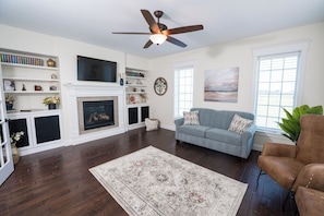 A living room with a fireplace, a ceiling fan, a television, and a sofa.