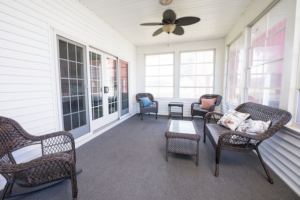 A covered patio area with wicker furniture, a ceiling fan, and large windows.