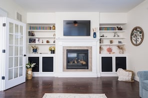 A living room with a fireplace, bookshelves, a television, and a wicker chair.
