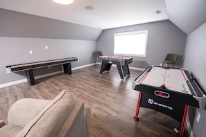 A room with a pool table, foosball table, and a bench.
