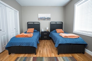 A bedroom with two beds, a nightstand, a window with blinds, and a door.
