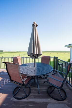 Ein runder Metalltisch mit vier Stühlen und einem Sonnenschirm auf einer Holzterrasse.