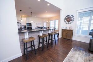 A spacious kitchen with a central island, bar stools, and a large wall clock.
